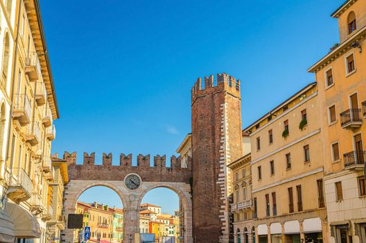 Portoni della Bra gate with merlons and clock, old Roman city double brick gate and medieval tower building in Verona historical centre, blue clear sky background, Veneto Region, Northern Italy