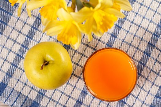 Good and delicious food and beverages for breakfast. Green apple, yellow daffodils and glass of orange juice on kitchen napkin. Top view