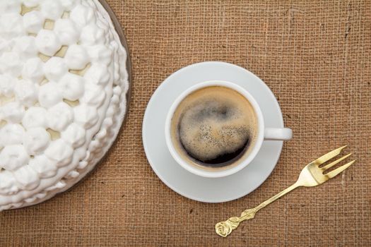 Biscuit cake decorated with whipped cream, cup of coffee and metal fork and cinnamon on table with sackcloth. Top view