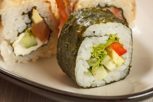 Close up Hosomaki with vegetables. Sushi roll with nori, rice, pieces of avocado, cucumber, red bell pepper and lettuce leaves and sushi rolls with Conger on the background. Japanese cuisine. Shallow depth of field