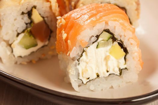 Close up Uramaki Philadelphia. Sushi rolls with salmon, nori, rice, Philadelphia cheese, pieces of avocado, cucumber on the dish. Japanese cuisine. Shallow depth of field