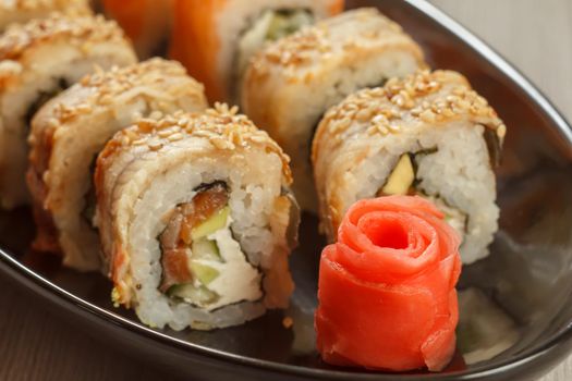 Close up pickled ginger in the form of red rose and sushi rolls - Uramaki with Conger on the background. Japanese cuisine. Shallow depth of field. Focus on ginger