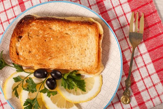 Good and delicious food and beverages for breakfast. Toast with butter and cheese, slices of lemon and olives on plate with fork on red kitchen napkin. Top view