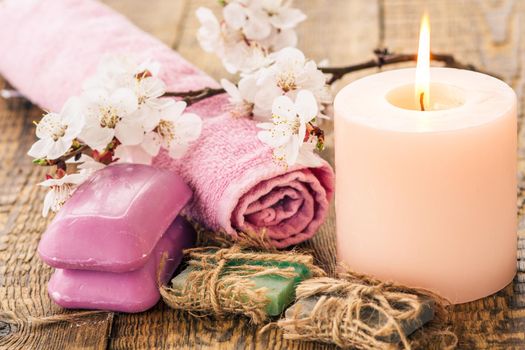 Handmade soap with towel for bathroom procedures and burning candle with flowering branch of apricot tree on the background. Spa products and accessories