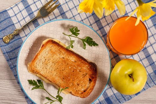 Good and delicious food and beverages for breakfast. Toast with butter and cheese, apple, bouquet of yellow daffodils and glass of orange juice on kitchen napkin. Top view