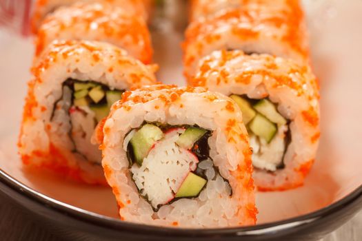 Close up Uramaki California. Sushi rolls with nori, rice, pieces of avocado, cucumber, crab sticks decorated with flying fish roe on ceramic plate. Japanese cuisine. Shallow depth of field