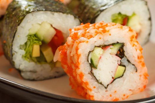 Close up Uramaki California. Sushi roll with nori, rice, pieces of avocado, cucumber, crab sticks decorated with flying fish roe and sushi rolls with vegetables on the background. Japanese cuisine. Shallow depth of field