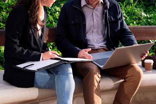 unrecognizable business partners working together with laptop in a park next to the office, concept of coworkers and remote work outdoors