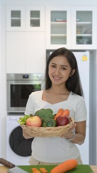 Portrait asian woman holding wicker basket with fresh organic vegetables and fruits standing in home office.