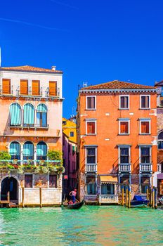 Grand Canal waterway in Venice historical city centre with gondolier on sailing gondola and Venetian architecture colorful buildings, blue sky in sunny day background. Veneto Region, Northern Italy.