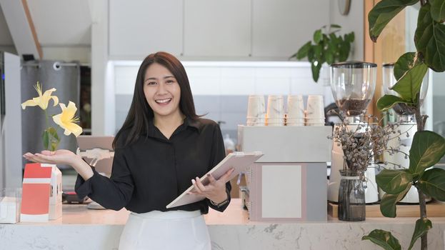 Successful female business owner standing in front of counter at her coffee shop and smiling at camera.