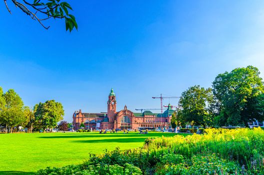 Wiesbaden Hauptbahnhof central railway station Neo-baroque style building and Reisinger-Anlagen park with green trees and lawn in historical city centre, blue sky background, State of Hesse, Germany