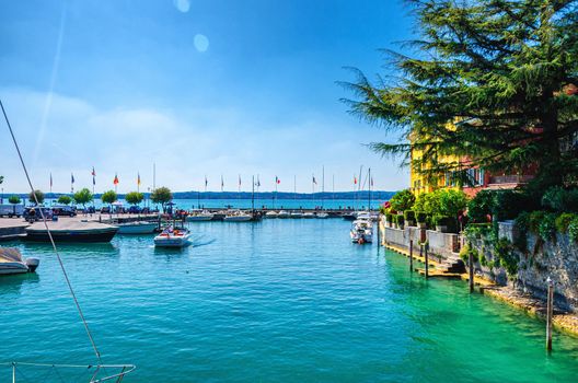 Harbour of Garda lake with blue azure turquoise water, wooden pier dock and yacht, motor boats, coast and blue sky background, Sirmione town, Lombardy, Northern Italy