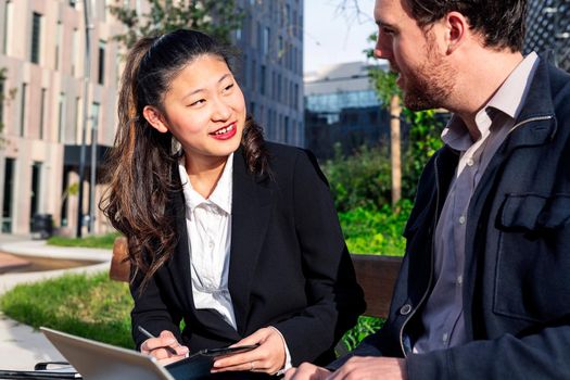 asiatic woman talking to her caucasian business partner while working in a park next to the office, concept of coworkers and diversity at work