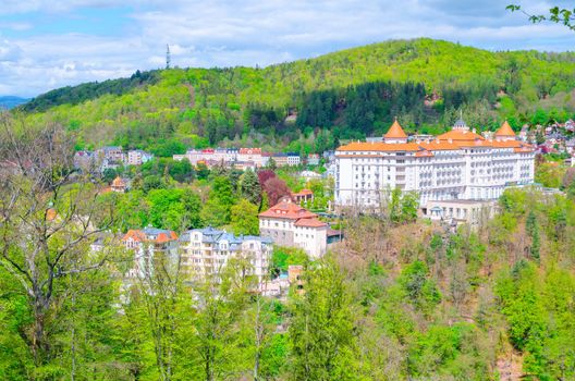 Karlovy Vary Carlsbad historical city centre top aerial view with hotels buildings, Slavkov Forest hills with green trees on slope, blue sky white clouds background, West Bohemia, Czech Republic
