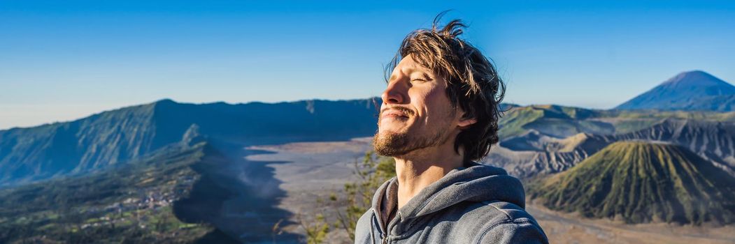 BANNER, LONG FORMAT Young man meets the sunrise at the Bromo Tengger Semeru National Park on the Java Island, Indonesia. He enjoys magnificent view on the Bromo or Gunung Bromo on Indonesian, Semeru and other volcanoes located inside of the Sea of Sand within the Tengger Caldera. One of the most famous volcanic objects in the world. Travel to Indonesia concept.