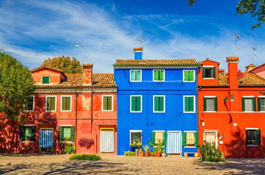 Colorful houses of Burano island. Multicolored buildings in small cobblestone square, blue sky background in sunny summer day, Venice Province, Veneto Region, Northern Italy. Burano postcard