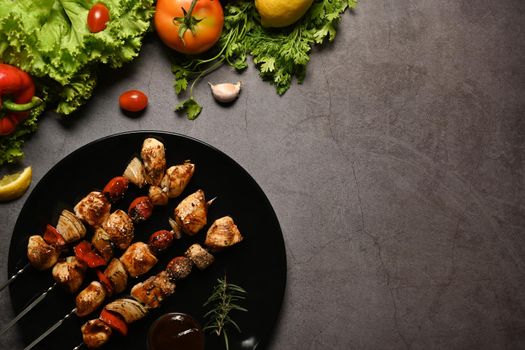 Delicious barbecue skewers with grilled chicken, cherry tomato, sweet pepper, onions and barbecue sauce on dark stone background.