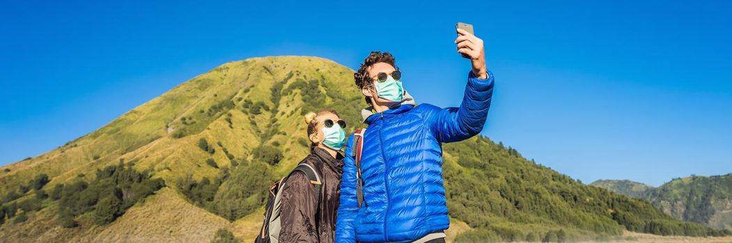 BANNER, LONG FORMAT Young man and woman tourists make a selfie in the Bromo Tengger Semeru National Park on the Java Island, Indonesia. They enjoy magnificent view on the Bromo or Gunung Bromo on Indonesian, Semeru and other volcanoes located inside of the Sea of Sand within the Tengger Caldera. One of the most famous volcanic objects in the world. Travel to Indonesia concept.