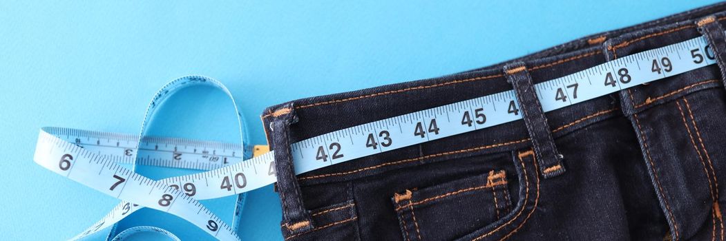 Measuring sewing tape lies on jeans on a blue background, close-up. Measurement of clothing size, tailoring and repair in the atelier