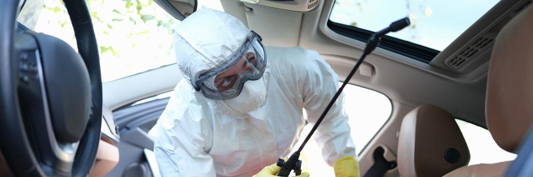 A man in protective clothing treats the interior of a car from the virus. Antibacterial protection during coronavirus