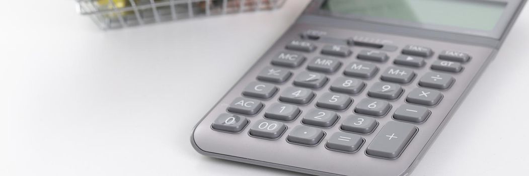 Calculator and basket with pills and capsules on a white background, close-up. Expenses for food supplements and vitamins, drug revenue