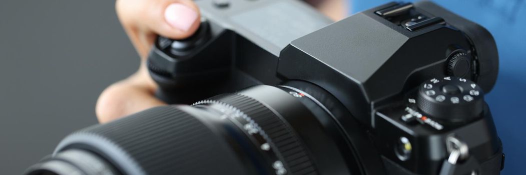 Woman holding a modern black camera for photographs, close-up. Digital device for photo studio and photographer, profession