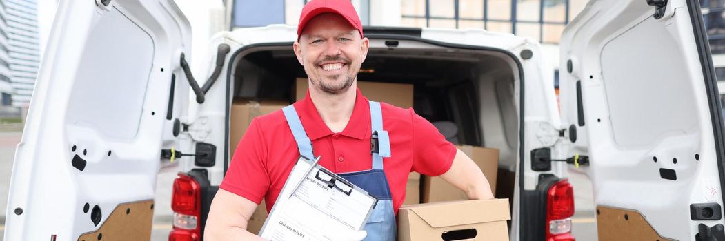 Smiling man holding a box and a delivery document, close-up. Business shipments, courier call. Logistic route