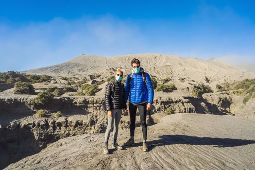 Young couple man and woman visit the Bromo volcano at the Tengger Semeru National Park on Java Island, Indonesia. They enjoy the magnificent view on the Bromo or Gunung Bromo on Indonesian, Semeru and other volcanoes located inside of the Sea of Sand within the Tengger Caldera. They wear safety masks to protect themselves from dangerous volcanic ash.