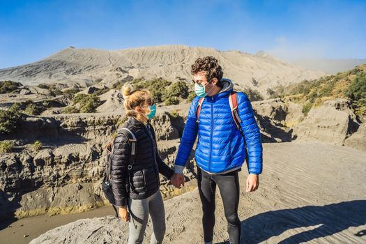 Young couple man and woman visit the Bromo volcano at the Tengger Semeru National Park on Java Island, Indonesia. They enjoy the magnificent view on the Bromo or Gunung Bromo on Indonesian, Semeru and other volcanoes located inside of the Sea of Sand within the Tengger Caldera. They wear safety masks to protect themselves from dangerous volcanic ash.