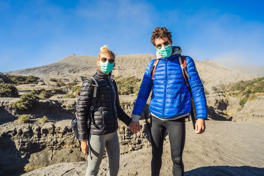 Young couple man and woman visit the Bromo volcano at the Tengger Semeru National Park on Java Island, Indonesia. They enjoy the magnificent view on the Bromo or Gunung Bromo on Indonesian, Semeru and other volcanoes located inside of the Sea of Sand within the Tengger Caldera. They wear safety masks to protect themselves from dangerous volcanic ash.