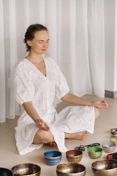 A woman sits with Tibetan bowls in the lotus position before doing yoga in the gym.