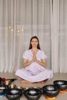 A woman sits with Tibetan bowls in the lotus position before doing yoga in the gym.