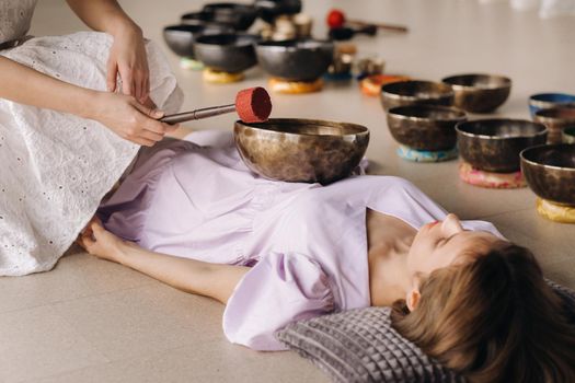 The copper singing bowl of the Nepalese Buddha in the spa. A young beautiful woman is doing a massage with singing bowls in a spa salon against the backdrop of a waterfall.