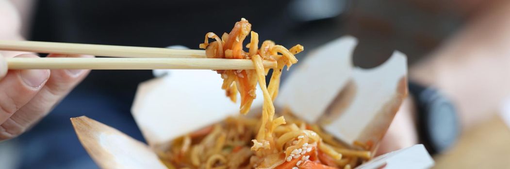 A man eats Chinese food from a box with wooden chopsticks, close-up. Traditional asian fast food, fresh delicious lunch