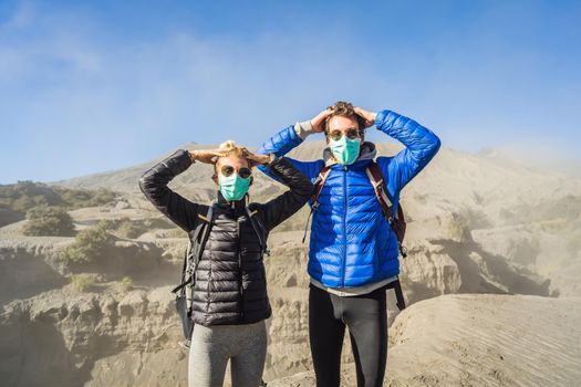 Young couple man and woman visit the Bromo volcano at the Tengger Semeru National Park on Java Island, Indonesia. They are scared of the eruption covering everything with dust and they wear safety masks to protect themselves from dangerous volcanic ash. Concept of tourists in trouble caused by a volcano.