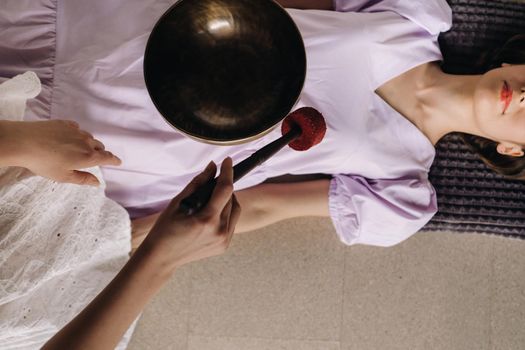 The copper singing bowl of the Nepalese Buddha in the spa. A young beautiful woman is doing a massage with singing bowls in a spa salon against the backdrop of a waterfall.