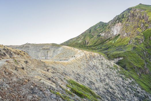 The magnificent views on green mountains from a mountain road trecking to the Ijen volcano or Kawah Ijen on the Indonesian language. Famous volcano containing the biggest in the world acid lake and sulfur mining spot at the place where volcanic gasses come from the volcano. Tourists hike this road to meet the sunrise at the volcano.
