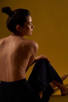 Back view of seductive woman with bare back sitting backwards on floor, with closed eyes. Brunette practicing yoga, stretching, bending. leaning forward. Concept of new age.