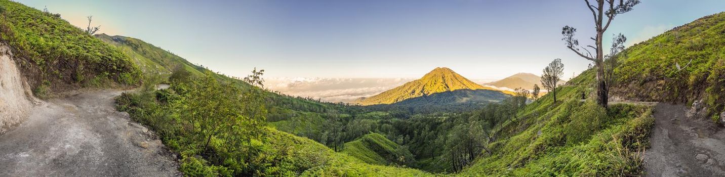 The magnificent views on green mountains from a mountain road trecking to the Ijen volcano or Kawah Ijen on the Indonesian language. Famous volcano containing the biggest in the world acid lake and sulfur mining spot at the place where volcanic gasses come from the volcano. Tourists hike this road to meet the sunrise at the volcano.