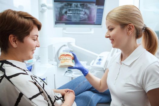 Cheerful female dentist showing her patient dental model with braces