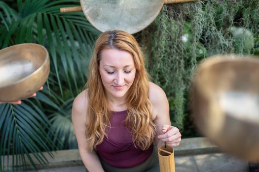 Yoga concept, meditation and sound therapy. Beautiful young caucasian woman surrounded by copper tibetan singing bowls and instruments