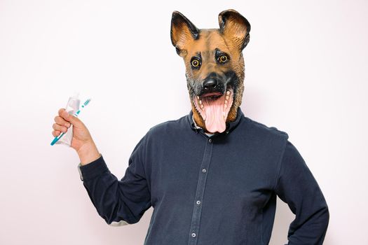 person with a dog mask holding toothbrush and toothpaste on white background, concept of dental care and hygiene for pets
