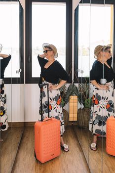 adventurous mature woman, arriving at the wardrobe of her summer holiday hotel room. businesswoman opening the wardrobe to leave her luggage. bedroom, natural light, dressing room with mirrors. copy space. vertical.