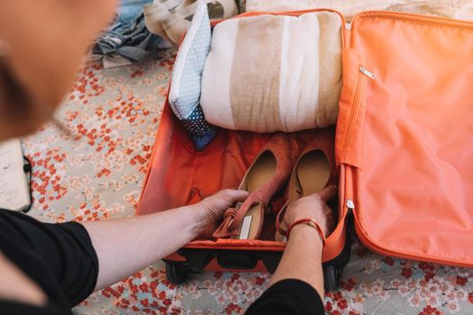 close-up of a suitcase being packed for a summer holiday. a woman's hands placing shoes in her luggage. travel and holiday concept. natural light, interior of a bedroom.