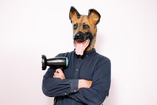 person wearing a dog mask with arms crossed and a hairdryer in his hand on white background, concept of hairdressing and grooming of pets