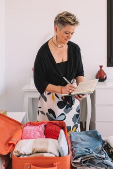 mature businesswoman, organising her luggage for a business trip. mature woman packing her suitcase for her holiday. bedroom room, natural light, clothes and travel items on the bed. vertical.