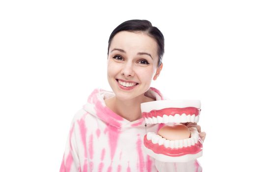 smiling woman in a pink hoodie holds a dental jaw in her hand, white background. High quality photo