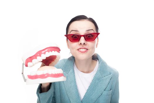 enthusiastic woman in red glasses and corduroy jacket holds a dental jaw in her hand, white background. High quality photo