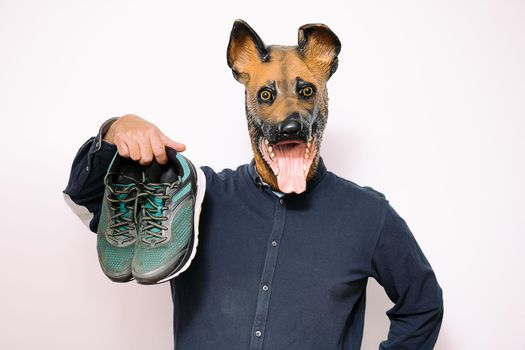 person with a dog mask holding a pair of running shoes on white background, concept of sport and active lifestyle with pets
